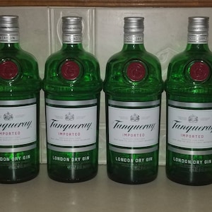 May include: Four green glass bottles of Tanqueray London Dry Gin. Each bottle has a silver cap, a white label with black text, and a red seal. The bottles are arranged side by side.