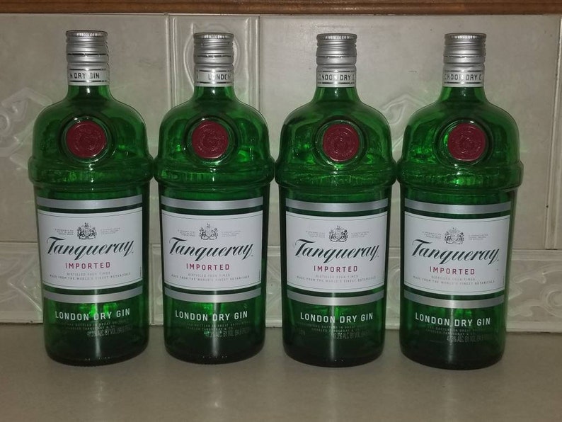 May include: Four green glass bottles of Tanqueray London Dry Gin. Each bottle has a silver cap, a white label with black text, and a red seal. The bottles are arranged side by side.