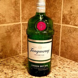 May include: A green glass bottle of Tanqueray London Dry Gin. The bottle has a white label with black text and a red seal. The bottle is 1 liter and 47.3% ABV.