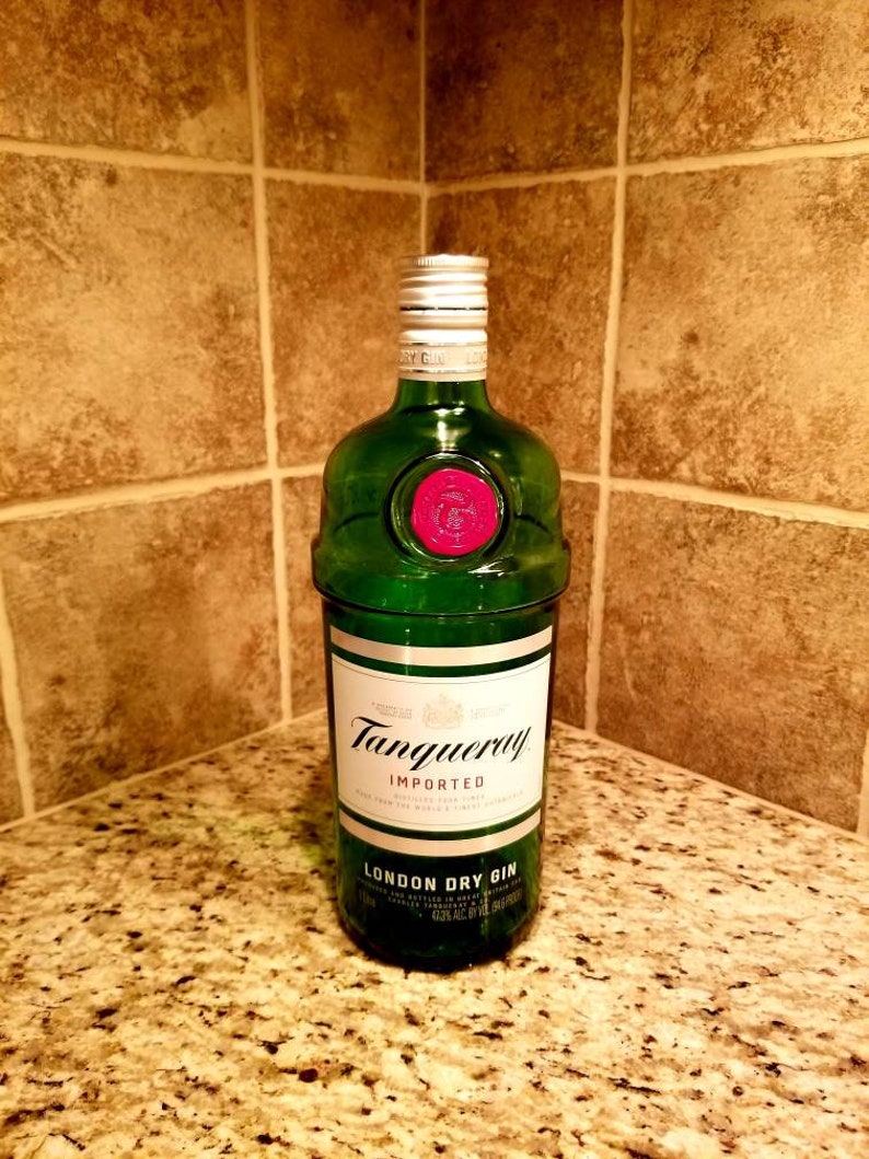 May include: A green glass bottle of Tanqueray London Dry Gin, with a white label and silver cap. The label reads "Tanqueray Imported London Dry Gin". The bottle has a red wax seal and is displayed on a speckled countertop.