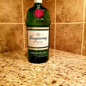 May include: A green glass bottle of Tanqueray London Dry Gin, with a red wax seal and a silver cap. The label reads "Tanqueray Imported London Dry Gin". The bottle is on a granite countertop.