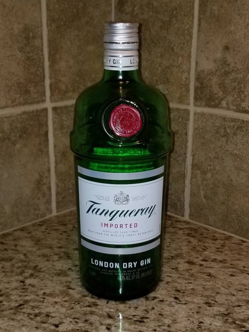 May include: A green glass bottle of Tanqueray London Dry Gin. The bottle has a silver cap and a white label with black text. The label reads "Tanqueray Imported London Dry Gin". A red seal is visible near the top of the bottle.