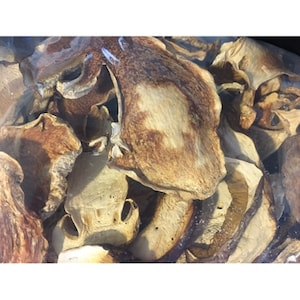 May include: Dried mushroom slices in a clear plastic bag. The mushrooms are light brown and have a slightly darker brown color in the center. The slices are various sizes and shapes.