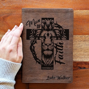 Könnte beinhalten: Ein braunes Lederjournal mit dem Schriftzug "Man of Faith" und einem Löwenkopf in einem Kreuz. Der Text "I Corinthians 16:13" und "Luke Walker" sind ebenfalls zu sehen.