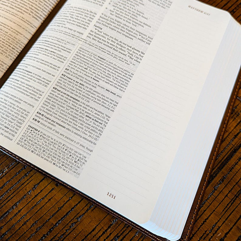Puede incluir: Biblia abierta con cubierta de cuero marr&oacute;n, mostrando texto en las p&aacute;ginas. Los bordes de las p&aacute;ginas son blancos y el libro est&aacute; abierto sobre una superficie de madera. El n&uacute;mero de p&aacute;gina 1251 es visible.