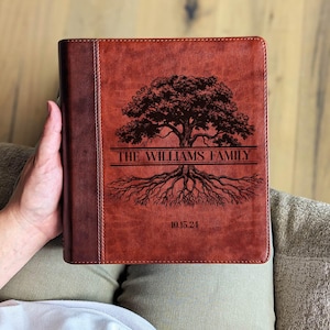May include: A brown leather journal with a tree design and the text "THE WILLIAMS FAMILY" and "10.15.24". The journal has a dark brown spine and is held by a person.