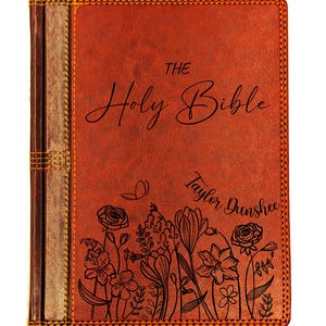 May include: A leather-bound Bible in a warm, reddish-brown hue. The cover features the words "The Holy Bible" in elegant script, along with the name "Taylor Dunshee." Delicate floral line art adorns the bottom of the cover, and the spine has a decorative stitch.