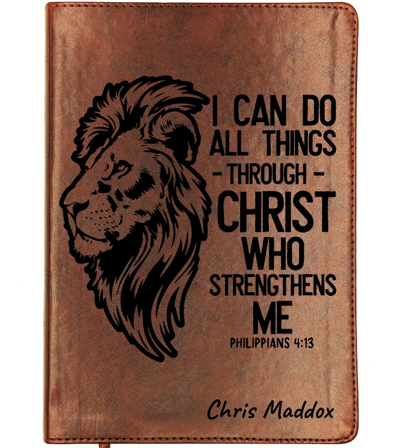 May include: A brown leather-bound journal with a black lion's head design and the text "I CAN DO ALL THINGS THROUGH CHRIST WHO STRENGTHENS ME" from Philippians 4:13. The name "Chris Maddox" is printed at the bottom.