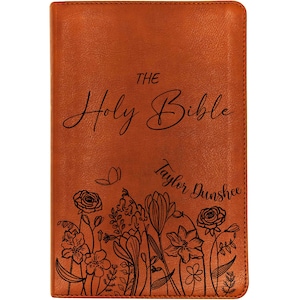 May include: A brown leather-bound Bible with the title "The Holy Bible" in elegant script. The cover features a floral design at the bottom and the name "Taylor Dunshee".
