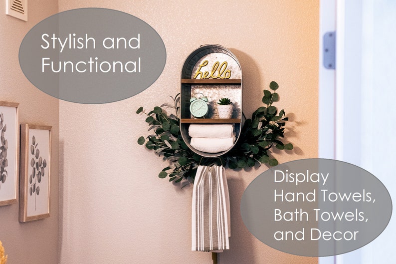 May include: A galvanised metal shelf with two shelves, a wooden top, and a metal sign that says "hello". The shelf is decorated with a green plant, a clock, and towels. The shelf is mounted on a wall with a white towel hanging below it.