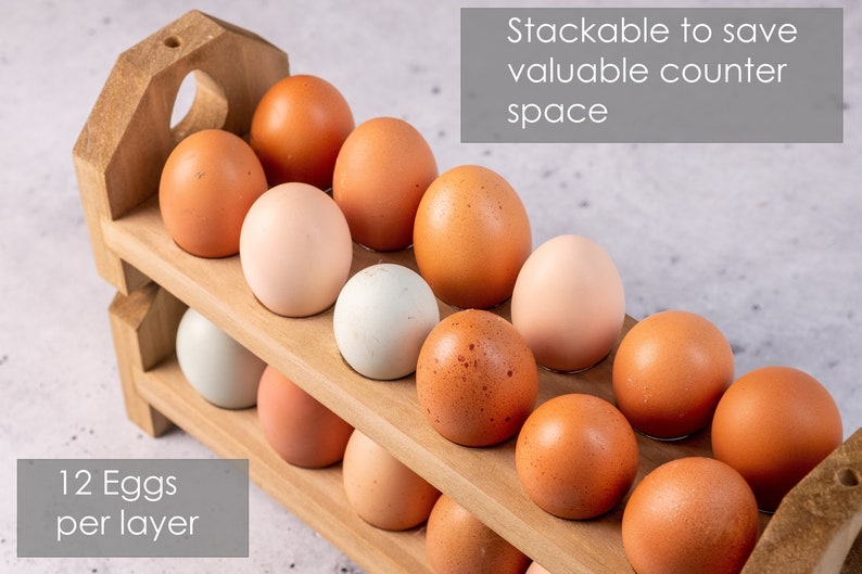 May include: A wooden egg holder with two tiers, each holding 12 eggs. The holder is made of natural wood and has a rustic look. The text "Stackable to save valuable counter space" is printed on a gray background above the holder. The text "12 Eggs per layer" is printed on a gray background below the holder.