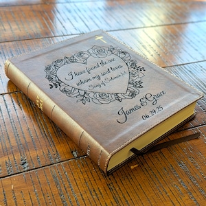 Może przedstawiać: Brązowa Biblia w sk&oacute;rzanej oprawie z złotym krzyżem i kwiatowym wzorem na okładce. Na okładce wygrawerowano tekst "I have found the one whom my soul loves Song of Solomon 3:4". Na okładce wygrawerowano r&oacute;wnież imiona "James & Grace" i datę "06.29.25".