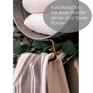 May include: A metal bucket with a brass handle, used as a towel holder. Two white towels are inside the bucket, and a striped towel is hanging from the handle. The text "Functional too, the Brass Handle serves as a Towel Holder" is visible in the image.