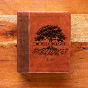 May include: A brown leather journal with a tree design and the text "THE WILLIAMS FAMILY" and "10.15.24". The journal has a darker brown spine and is stitched with white thread.