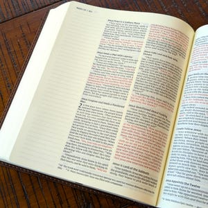 Może przedstawiać: Zbliżenie na brązową, sk&oacute;rzaną Biblię otwartą na Księgę Marka, rozdział 1, wersety 35-45. Tekst jest podświetlony na czerwono i opowiada o uzdrowieniu trędowatego przez Jezusa oraz o przebaczeniu i uzdrowieniu sparaliżowanego mężczyzny.