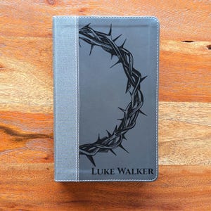May include: Gray Bible cover with a black crown of thorns design. The spine is a lighter gray fabric with white stitching. The name "LUKE WALKER" is printed in white at the bottom of the cover.