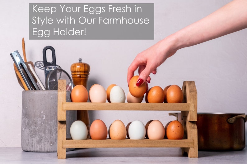 May include: A two-tiered wooden egg holder with brown eggs and blue eggs on each shelf. The egg holder is on a white countertop with a gray concrete utensil holder and a brown pot in the background. The text "Keep Your Eggs Fresh in Style with Our Farmhouse Egg Holder!" is at the top of the image.
