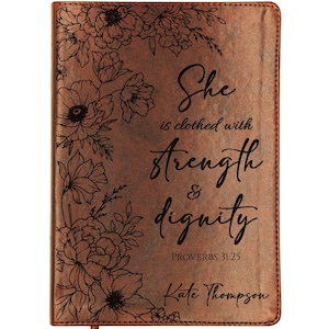 May include: A brown leather-bound journal with floral illustrations and the text "She is clothed with strength & dignity PROVERBS 31:25 Kate Thompson". The journal has a ribbon bookmark.