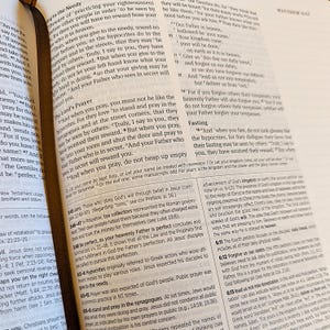 Puede incluir: Biblia abierta con texto de Mateo 6:1-17, sobre la oraci&oacute;n y la justicia. Las p&aacute;ginas est&aacute;n amarillentas, con una cinta de marcador marr&oacute;n. El texto es negro, con algunas anotaciones.