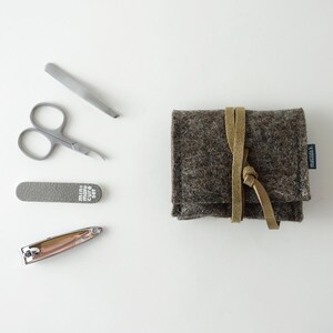 May include: A brown felt pouch with a leather strap and the word "matildal."  The pouch contains a set of manicure tools including a nail clipper, nail file, tweezers, and nail scissors.
