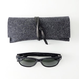 May include: Black sunglasses with a gray felt case and a black leather strap. The sunglasses have a classic wayfarer style.