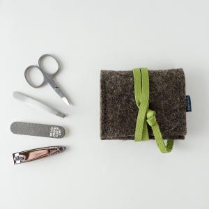 May include: A brown felt pouch with a green strap, containing a mini manicure set. The set includes a nail clipper, nail file, tweezers, and small scissors.