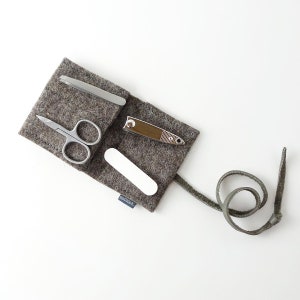 May include: A gray felt pouch with a leather strap, containing a nail clipper, nail file, tweezers, and small scissors. The pouch has the text "mail&co." printed on it.
