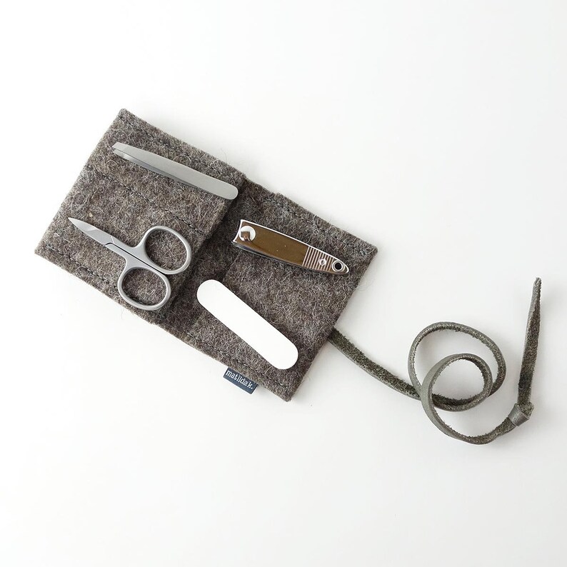 May include: A gray felt pouch with a leather strap, containing a nail clipper, nail file, tweezers, and small scissors. The pouch has the text "mail&co." printed on it.