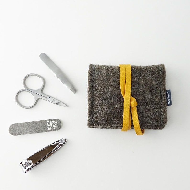May include: A gray felt pouch with a yellow ribbon closure. The pouch contains a nail clipper, tweezers, a nail file, and a pair of small scissors. The pouch has the text "mini manicure set" printed on the front.