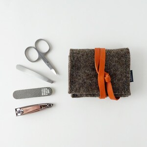 May include: A brown felt pouch with a brown leather strap and a small nail clipper, nail file, tweezers, and scissors. The pouch has the text "mini mani cure set" printed on the front.