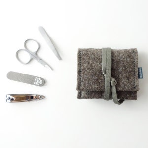 May include: A gray felt pouch with a brown leather strap and the word "marimekko" printed on the side. The pouch contains a nail clipper, a nail file, tweezers, and a pair of nail scissors.