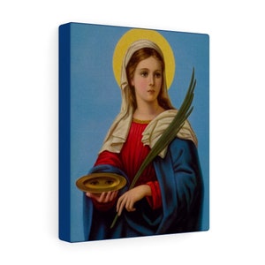 May include: A painting of a woman in a blue and red robe holding a golden plate with a face on it. She is wearing a white veil and has a halo around her head. She is holding a branch of leaves in her other hand.