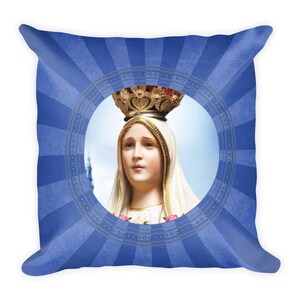 Può includere: Un cuscino blu con un designo circolare che presenta una rappresentazione della Madonna di Fatima. L'immagine la mostra con un velo bianco e una corona, con un cielo blu e nuvole sullo sfondo.