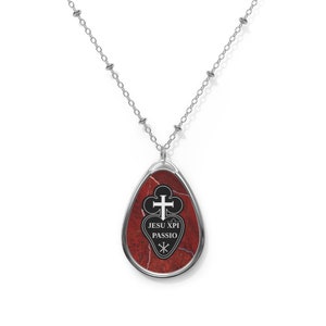 May include: A silver chain necklace with a red and black teardrop-shaped pendant. The pendant features a cross and the text "JESU XPI PASSIO".