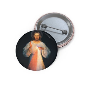 Può includere: Un bottone con un dipinto di Gesù Cristo con un cuore raggiante. Il cuore è circondato da raggi di luce rossi, arancioni, gialli e bianchi. Lo sfondo è nero.
