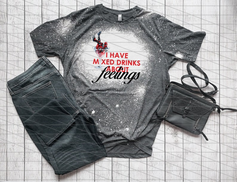 May include: A gray t-shirt with a graphic of a cocktail and the text "I HAVE MIXED DRINKS ABOUT feelings". The shirt is paired with dark wash jeans and a black purse.
