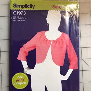 May include: A Simplicity sewing pattern package, C1973, featuring a pink bolero jacket design. The package includes size information and the text "one easy project" on a purple background.