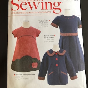 May include: A sewing pattern titled "Classic Sewing" for everyday and special occasions. The pattern features three children's garments: a red dress with an apple applique, a navy blue dress with tartan trim, and a navy blue jacket with red buttons and tartan trim.