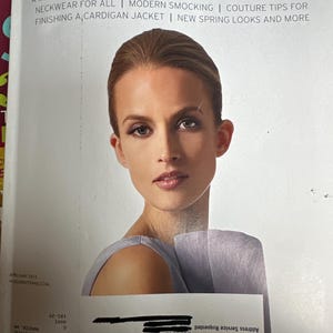 May include: The cover of Vogue Patterns magazine, featuring a woman with light skin and brown hair. The magazine's title is in large, blue letters. Text includes "A MAN WHO EMBROIDERS WITH FURY..." and "THE ULTIMATE SEWING MAGAZINE."