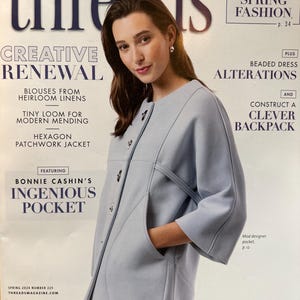 May include: The cover of Threads magazine shows a woman in a pale blue coat. The magazine's title is at the top, with text about spring fashion and sewing projects. The cover also highlights articles on alterations and a clever backpack.