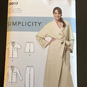 May include: A Simplicity sewing pattern envelope featuring a woman in a beige robe and pajama set. The envelope includes illustrations of the robe, short-sleeved shirt, long-sleeved shirt, shorts, and pants. The pattern size is S-XXXL.