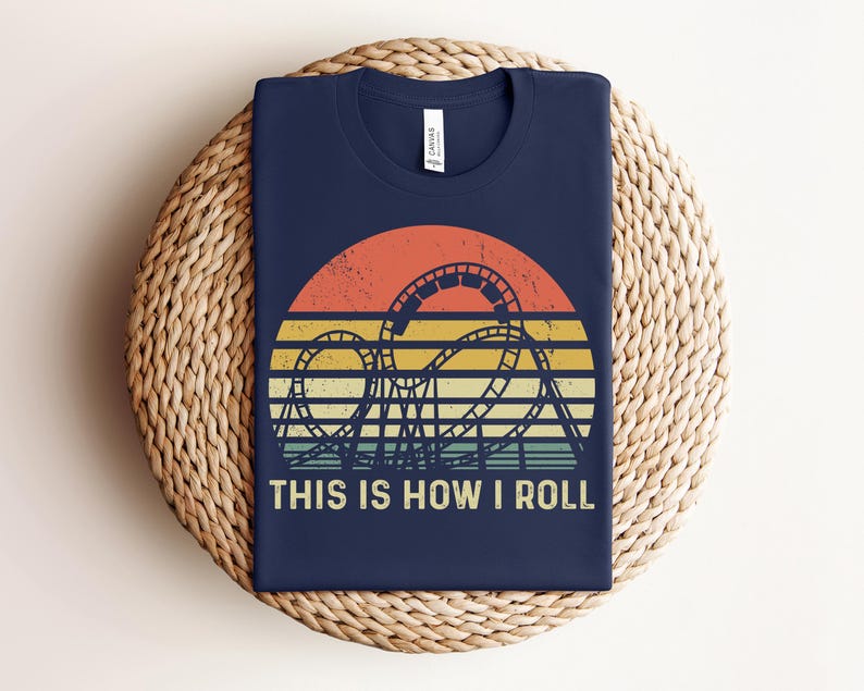 Może przedstawiać: Granatowa koszulka z nadrukiem w stylu retro z zachodem słońca i sylwetką kolejki g&oacute;rskiej. Pod grafiką znajduje się napis "THIS IS HOW I ROLL". Koszulka wykonana jest z miękkiego materiału.