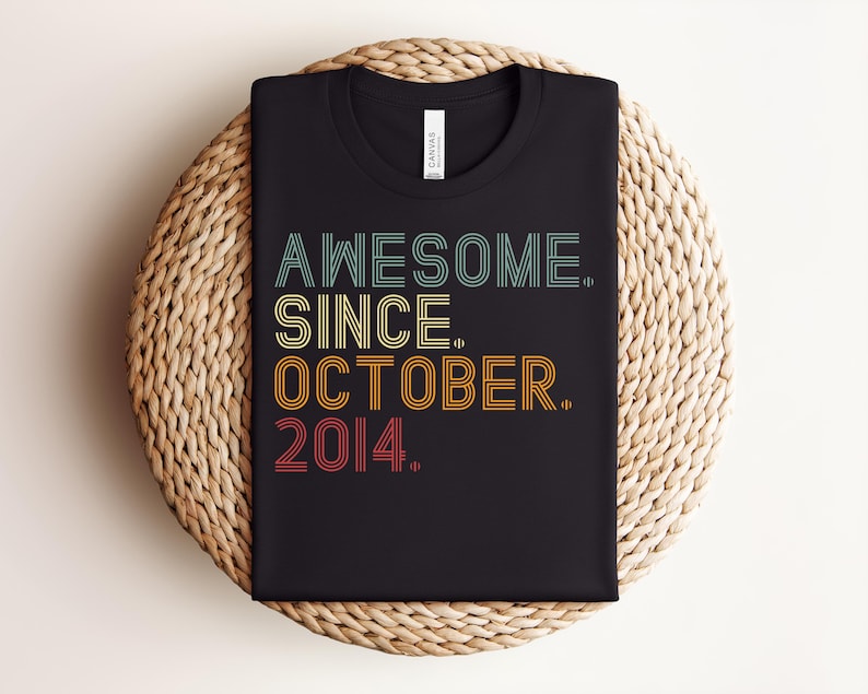 Puede incluir: Una camiseta negra de manga corta con el texto AWESOME. SINCE. OCTOBER. 2014. impreso en una fuente de estilo retro de varias l&iacute;neas con detalles de l&iacute;neas horizontales. Los colores del texto son azul claro, amarillo, naranja y rojo.