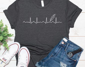 Könnte beinhalten: Ein dunkel anthrazitfarbenes Kurzarm-T-Shirt mit einem weißen Grafikdruck einer Herzschlaglinie, die eine Feder integriert. Das T-Shirt wird zusammen mit einer blauen Jeansshorts und weißen Canvas-Sneakern präsentiert.