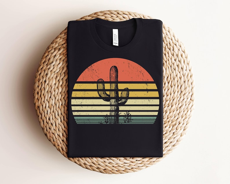 May include: Black t-shirt with a retro sunset graphic featuring a tall cactus in the center. The sunset is in shades of orange, yellow, and blue.