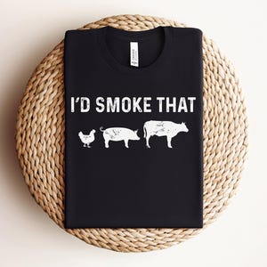 K&ouml;nnte beinhalten: Schwarzes T-Shirt mit dem Text "I'd Smoke That" in wei&szlig;en Buchstaben. Das Shirt zeigt eine wei&szlig;e Silhouette eines Huhns, eines Schweins und einer Kuh.