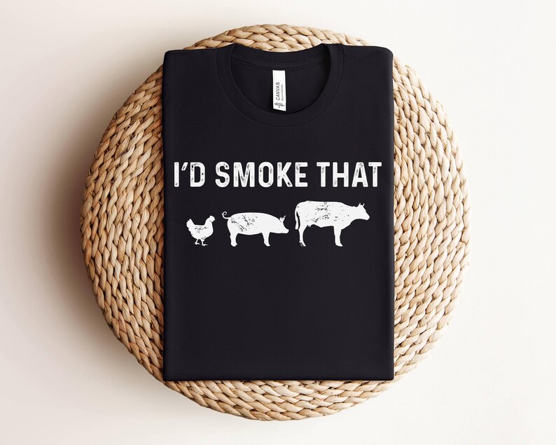 K&ouml;nnte beinhalten: Schwarzes T-Shirt mit dem Text "I'd Smoke That" in wei&szlig;en Buchstaben. Das Shirt zeigt eine wei&szlig;e Silhouette eines Huhns, eines Schweins und einer Kuh.