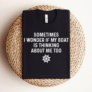 May include: Black t-shirt with white text that reads "Sometimes I wonder if my boat is thinking about me too." A white steering wheel icon is below the text.