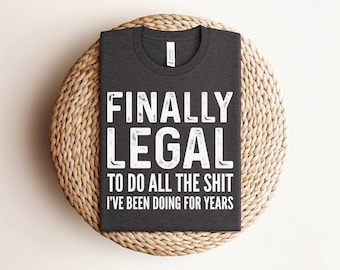 Op de afbeelding: Een donkergrijs t-shirt met ronde hals en witte letters in een verweerde stijl met de tekst FINALLY LEGAL TO DO ALL THE SHIT I'VE BEEN DOING FOR YEARS. Het t-shirt heeft een standaard model met korte mouwen en een wit merklabel in de nek.