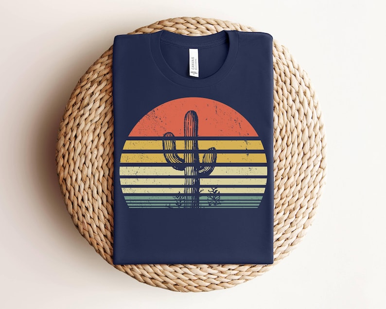 May include: A navy blue t-shirt with a retro sunset graphic featuring a silhouette of a cactus. The sunset is in shades of orange, yellow, and blue.